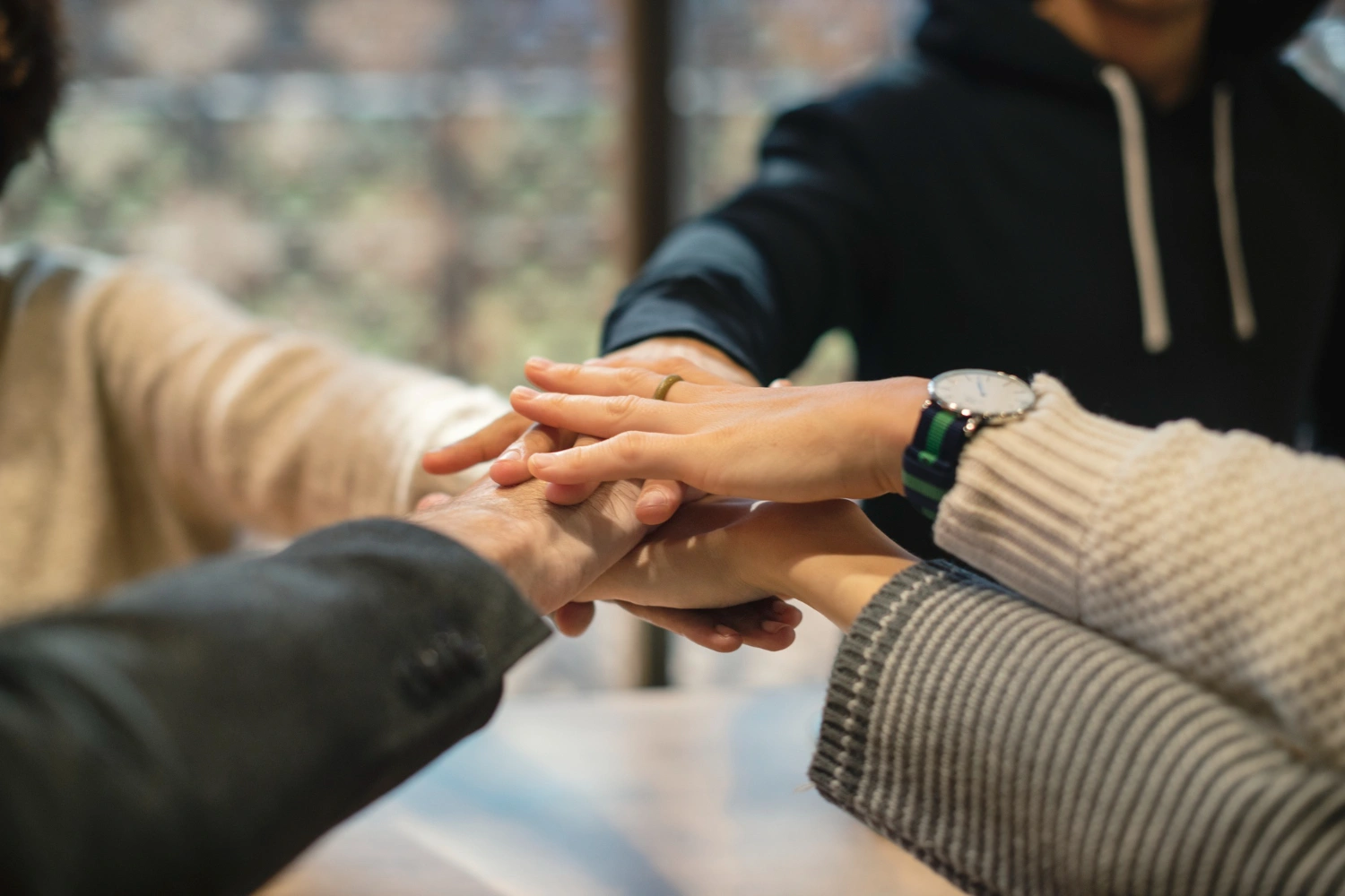 Four people stacking their hands together in a gesture of teamwork and unity.