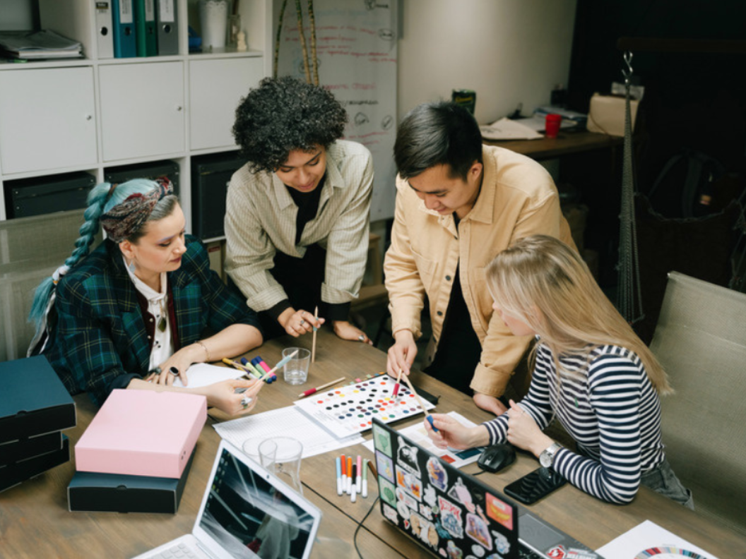 Several people gathered around a table with a laptop and papers, planning together.