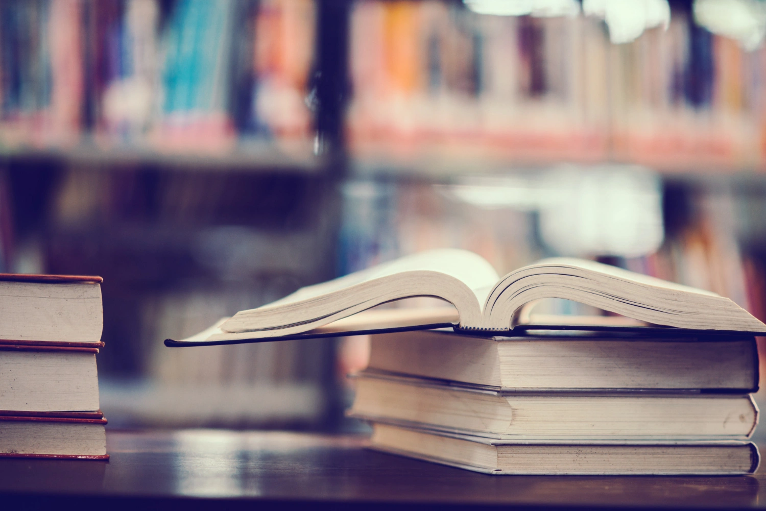 An open book resting on top of a stack of books in a library.