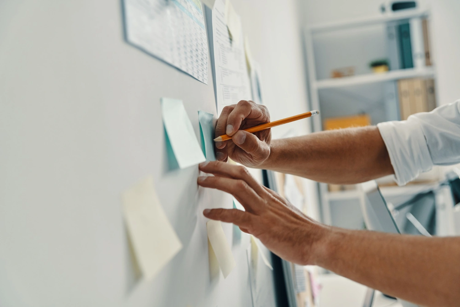 Person writes on a sticky note on a whiteboard, surrounded by other sticky notes and papers.